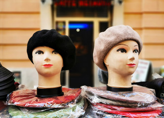 Woman heads dummies wearing fashion caps, a black one and a beige one, stylish dummy models in an outdoors market retail commerce shop stall on an urban building wall background with horizontal lines