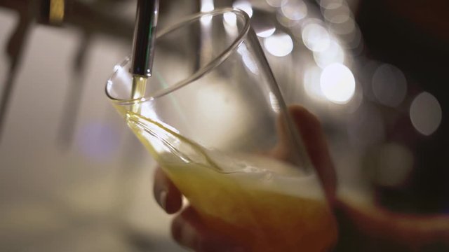 pouring beer with bubbles and foam in glass from tap with hand holding it, angle side view, slow motion