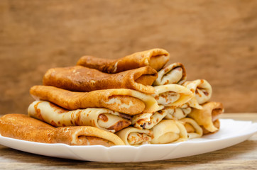 Pancakes with filling stacked pyramid on a white plate, standing on a wooden background close-up