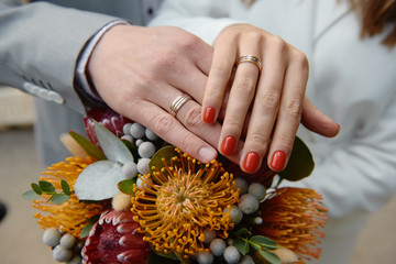 Newlywed couple's hands with wedding rings on bridal bouquet of protea, copy space. Wedding couple,...