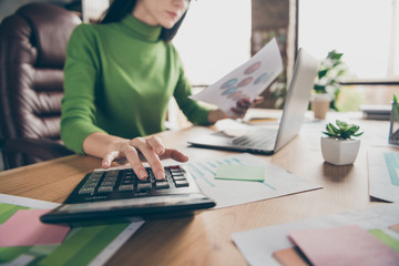 Cropped closeup photo of busy business lady notebook table hold paper stats calculating numbers sums money income sit chair wear green turtleneck modern office