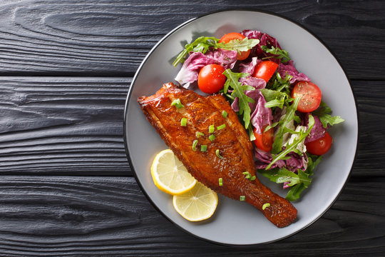 Main dish fried rockfish served with fresh vegetable salad close-up in a plate. horizontal top view
