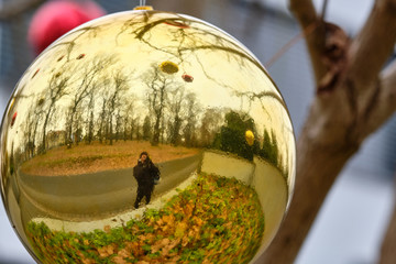 Closeup of a big golden Christmas bauble hanging in a tree in a garden and reflecting the surroundings like the street, trees and the photographer. Seen in Bavaria, Germany in December