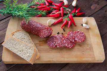 Smoked sausage sliced into pieces, slices of garlic and red chili peppers on a dark background. Not a healthy diet. The concept of cooking.