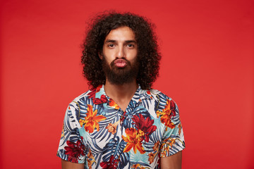 Funny portrait of young dark haired curly man with beard making ridiculous faces while posing...