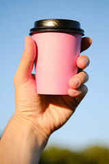 Human hand holds paper pink glass with coffee on blue background. Coffee to go, take-away coffee.