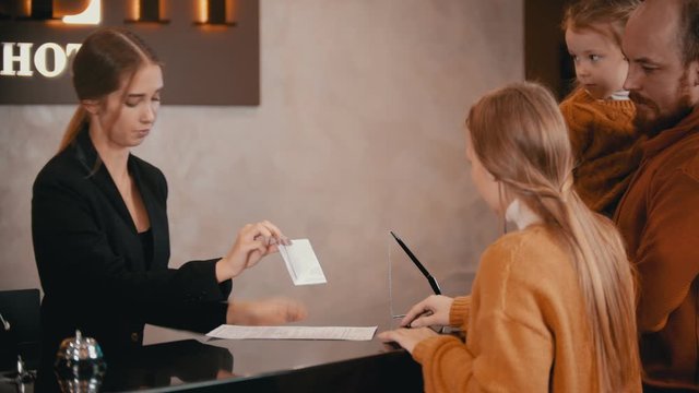 A family checking in the luxury hotel - a woman on the reception explains to the family their privileges in the hotel and gives a brochure and keys to them