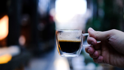 Transparent glass cup of coffee in the hand. Coffee in a cafe. 