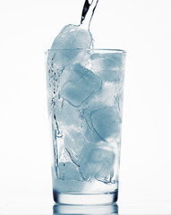 pouring water in a glass full of ice cubes, white background, blue toned object