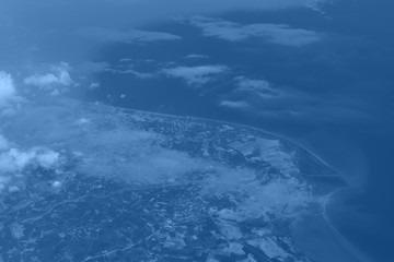 Fototapeta na wymiar Top view from landing airplane in trendy monochrome blue and calm color background. Window plane with copy space. Aerial view of cloud, sea, ocean and city landscape