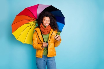 Photo of beautiful dark skin lady hold colorful umbrella reading email telephone modern blogger wear overcoat jeans green sweater scarf isolated blue color background © deagreez