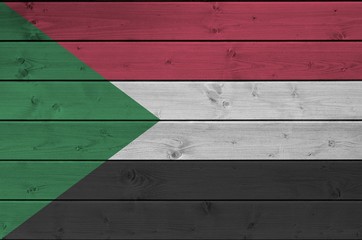 Sudan flag depicted in bright paint colors on old wooden wall. Textured banner on rough background