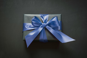 Gift box wrapped in black paper with classic blue ribbon on black surface. Trendy color of the 2020 Year.