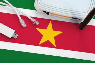 Suriname flag depicted on table with internet rj45 cable, wireless usb wifi adapter and router....