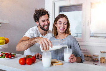 Young cheerful couple having fun during breakfast time in the kitchen. Cheerful young man hugging...