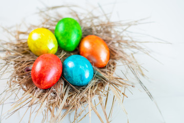 Multi-colored Easter eggs lie together on a straw in the form of a nest on a white background. Happy easter