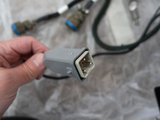 A man holds rare metal square cable connector in his hand. Very shallow depth of field DOF. Blurred background.