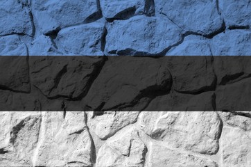 Estonia flag depicted in paint colors on old stone wall closeup. Textured banner on rock wall...