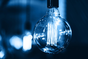 Close-up of a round huge light bulb toned in blue trend color against a dark background in the...