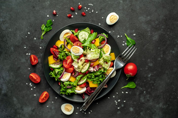 Salad with pomegranate, eggs, tomatoes, fresh cucumbers, onions, sesame and bell pepper, spices on a stone background. Healthly food.