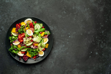 Salad with pomegranate, tomatoes, fresh cucumbers, onions, sesame seeds and cashew nuts, spices on a stone background. Healthy vegetarian food. 