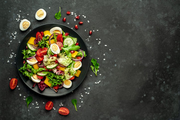 Salad with pomegranate, tomatoes, fresh cucumbers, onions, sesame seeds and cashew nuts, spices on a stone background. Healthy vegetarian food. 
