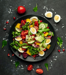Salad with pomegranate, eggs, tomatoes, fresh cucumbers, onions, sesame and bell pepper, spices on a stone background. Healthly food.