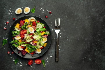 Salad with pomegranate, eggs, tomatoes, fresh cucumbers, onions, sesame and bell pepper, spices on a stone background. Healthy food. With copy space for your text.