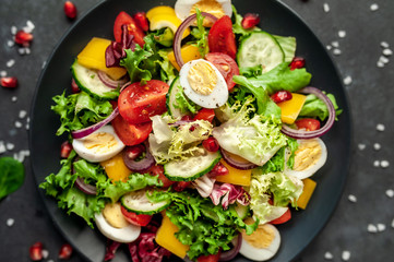 Salad with pomegranate, eggs, tomatoes, fresh cucumbers, onions, sesame and bell pepper, spices on a stone background. Healthly food.