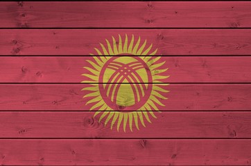 Kyrgyzstan flag depicted in bright paint colors on old wooden wall. Textured banner on rough...