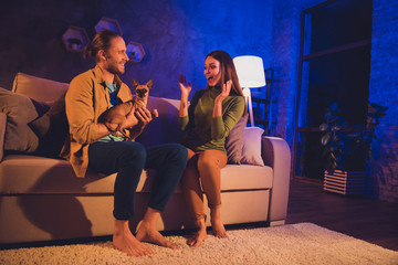 Naklejka premium Portrait of his he her she nice attractive cheerful cheery glad spouses sitting on divan guy giving toy terrier to girl on 25 December Eve Noel at night home house living-room apartment