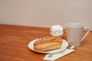 Tea, two eclairs and a custard cake on a wooden table with a light background