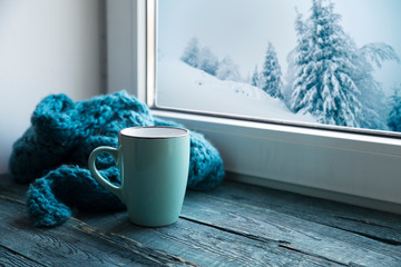Winter background - cup with candy cane, woolen scarf and gloves on windowsill and winter scene...