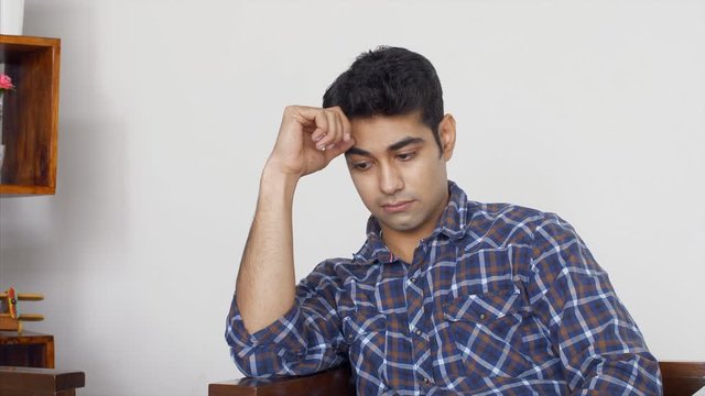 A stressed young Indian man sitting on the sofa. 4K Stock Footage of a young Indian man having sad thoughts and feeling upset