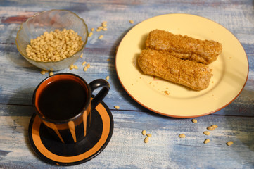 Two cakes on a plate, pine nuts and a mug of coffee on a wooden background.