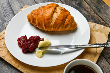 Kurasan with butter and jam. the beginning of the morning. A cup of coffee. Fresh french croissant. Coffee cup and fresh baked croissants on a wooden background. View from above.