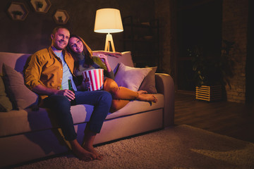 Fototapeta Nice attractive lovely cheerful cheery couple girl sitting on divan enjoying snack watching film spending day weekend holiday at night dark home house apartment indoors obraz