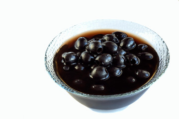 Black olives lie in a glass vase isolated on white background