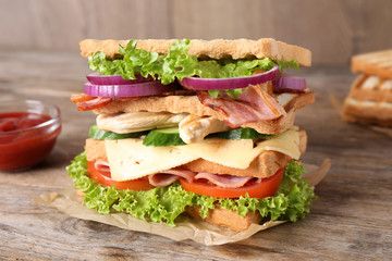 Tasty sandwich with chicken, ham and bacon  on wooden table