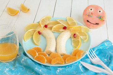 Funny cute Breakfast for kids with imitation of sea, sun, beach with palm trees. food background, carving. on a blue plate is a palm tree made from slices of lemon, banana, Mandarin and pomegranate.