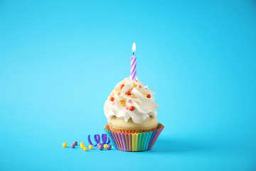 Delicious birthday cupcake with candle on light blue background