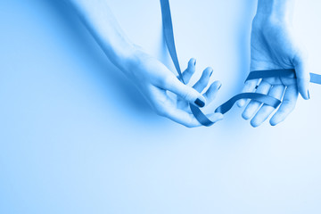 Classic blue, toned image. young female hands holding red ribbon, palm with nail polish on it, self and health care, copy space on aquamarine background top view