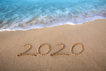 Fototapeta na wymiar New Year 2020 is coming concept. 2020 inscription written in the wet beach sand with sea water wave