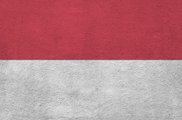 Monaco flag depicted in bright paint colors on old relief plastering wall. Textured banner on rough...