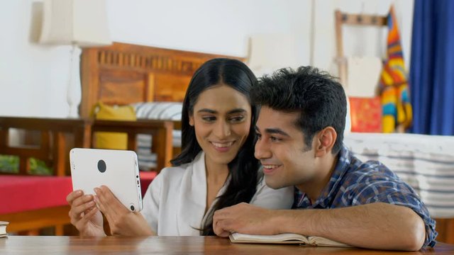 Young Indian couple video chatting on their tab sitting together in their bedroom. Indian Stock Footage of a beautiful married couple in a video conference call with their friends / grandparents