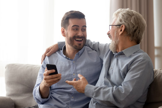 Different generations relatives men using smartphone laughing sit on couch