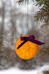 candied orange Christmas ball hanging on a tree against the background of a winter forest and snowfall. soft focus