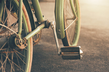 On the asphalt stands a green old retro bike with rusty parts and a chain, illuminated by a...