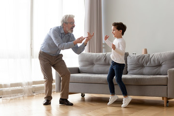 Full-length grandfather dancing with little grandson at home