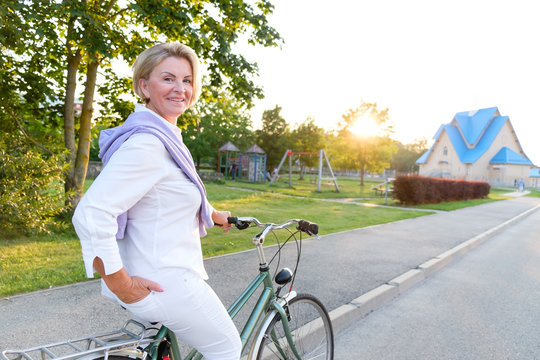 Old People, Leisure And Lifestyle Concept - Portrait Of Senior Woman 60-65 Years Old On Bicycle. Older Lady Riding City Bike In European Town. 